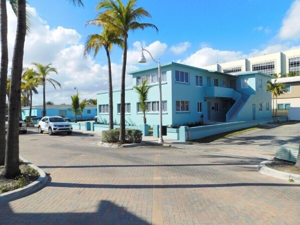A modern building with a blue facade, a parking area, and palm trees.