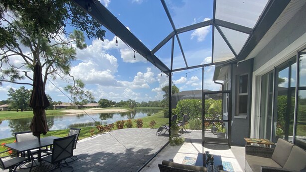 A covered patio with outdoor furniture, a view of a lake, and a golf course in the background. - Relax on your lanai after a round of golf and enjoy our beautiful SWFL sunsets! (Fort Myers)