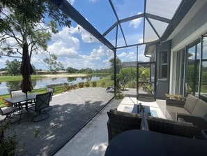 Un patio cubierto con mobiliario exterior, vista a un lago y un campo de golf al fondo.