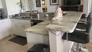 A modern kitchen with a marble countertop, a sink, and a dining area with bar stools. - Relax on your lanai after a round of golf and enjoy our beautiful SWFL sunsets! (Fort Myers)