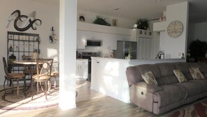 A modern kitchen with white cabinets, a stainless steel refrigerator, and a microwave. There is a dining area with a round table and chairs. - Relax on your lanai after a round of golf and enjoy our beautiful SWFL sunsets! (Fort Myers)