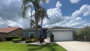 A residential house with a garage, a lawn, and a palm tree. - Relax on your lanai after a round of golf and enjoy our beautiful SWFL sunsets! (Fort Myers)