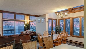 Ein gemütlicher Essbereich mit einem Holztisch und Stühlen, einer braunen Ledersofa und großen Fenstern mit Blick ins Freie.