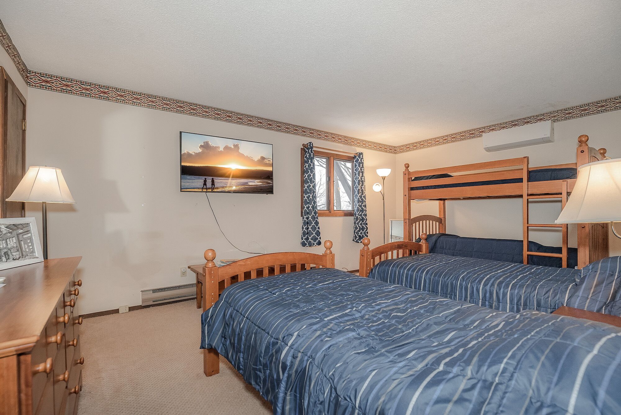 A bedroom with two bunk beds, a desk, a chair, a lamp, and a picture of a sunset.