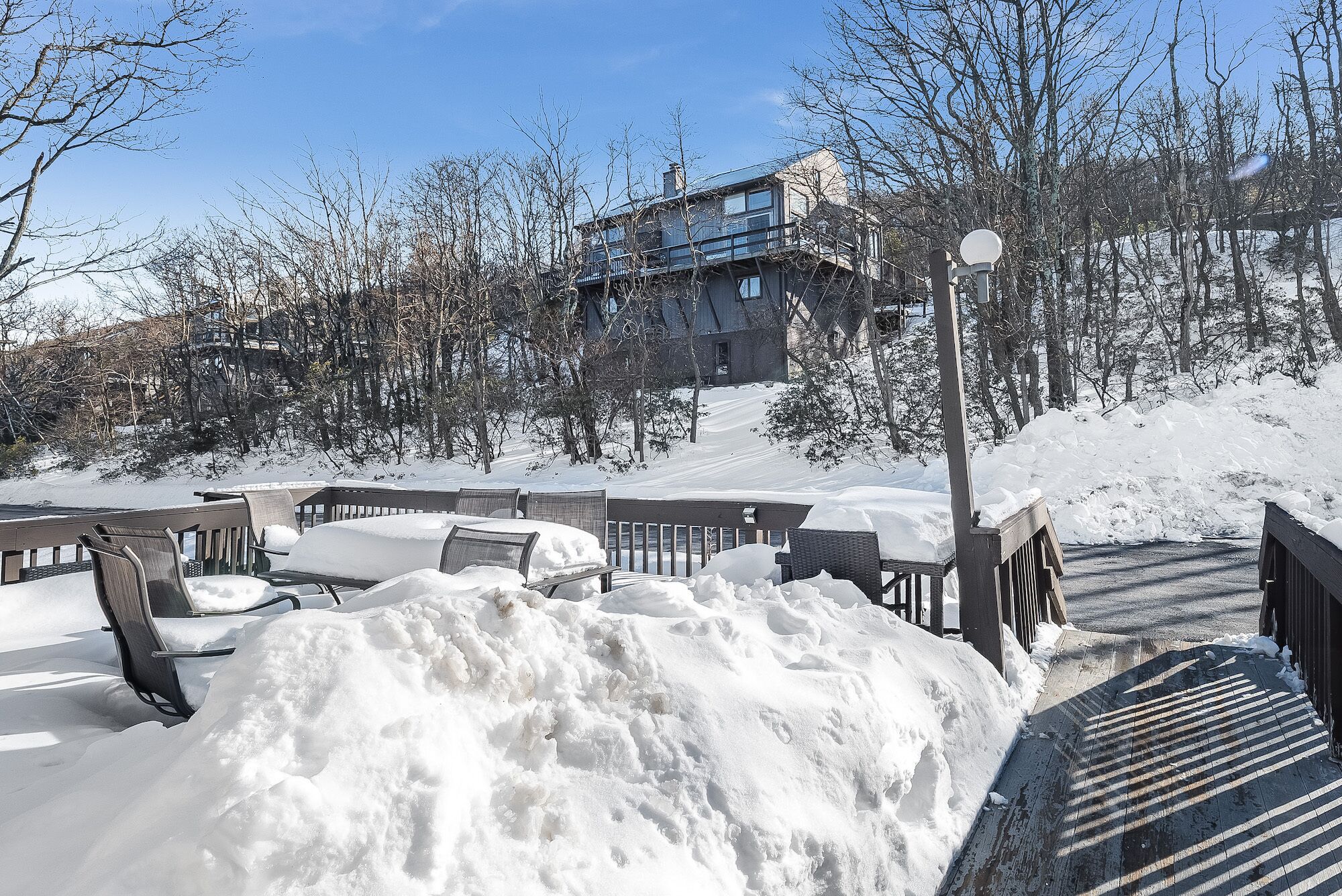 A snow-covered outdoor seating area with benches and a wooden deck, leading to a building with a balcony.