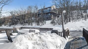 A snow-covered outdoor seating area with benches and a wooden deck, leading to a building with a balcony.