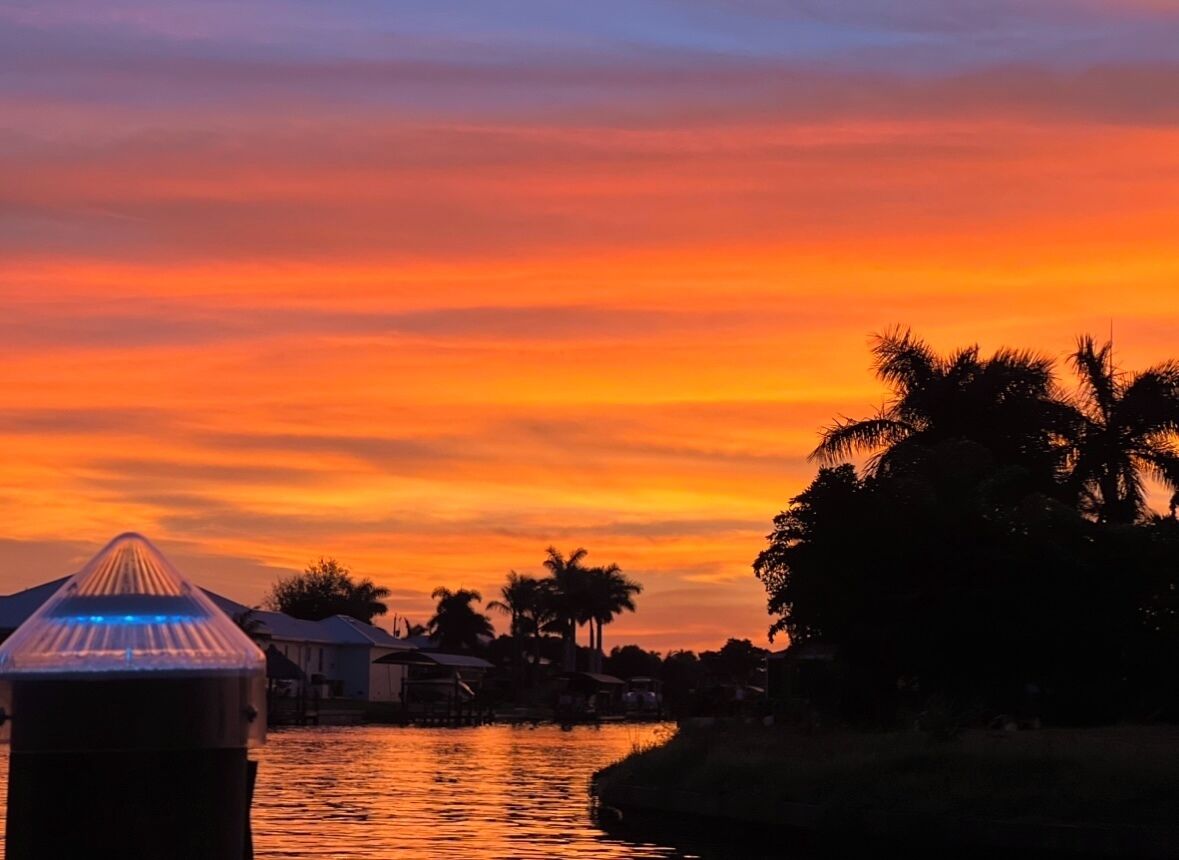 A sunset over a body of water with palm trees and houses in the background.