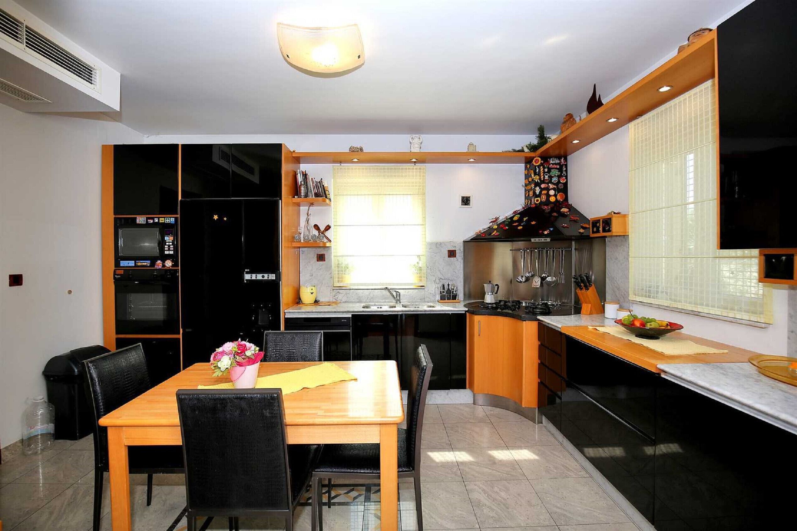 A modern kitchen with built-in appliances, a dining area with a wooden table and chairs, and a large window providing natural light.