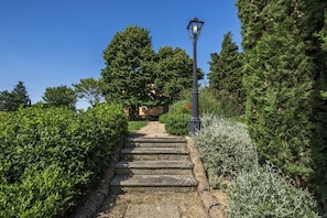 Eine steinerne Treppe führt zu einem Gebäude mit einer Straßenlaterne, umgeben von dichtem Grün.
