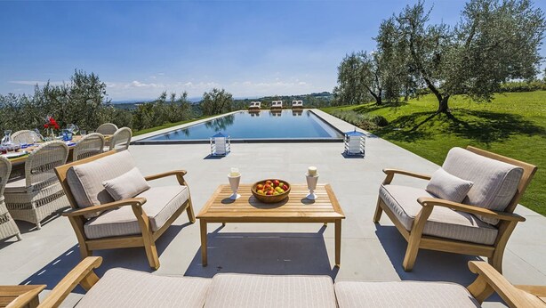 An outdoor pool area with lounge chairs, a table with a fruit bowl, and a view of the landscape. - Villa Miniato by MMega (San Miniato)