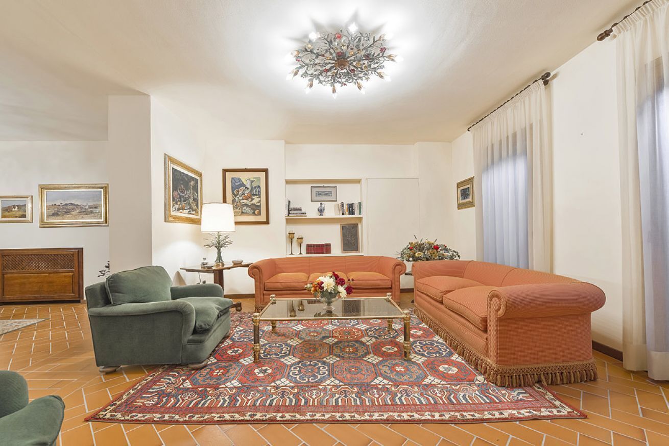 Una sala de estar con sofá, sillones, una mesa de centro, alfombra estampada y candelabro.