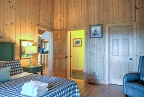 Ein Zimmer mit Bett, Stuhl, Tür und einem kleinen Tisch mit Lampe.