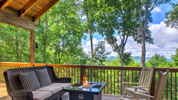 A covered deck with a glass-top fire feature, wicker sofa, and a white chair.