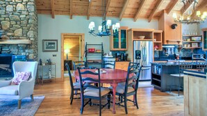 A spacious living area with a stone fireplace, wooden ceiling, and a dining table surrounded by chairs.