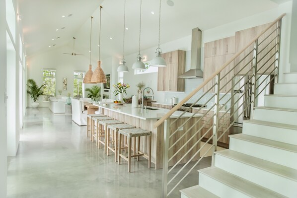 A modern kitchen with a central island, bar stools, pendant lighting, and a staircase with a wooden finish. - Location, comfort, and 5 beach accesses to more than one mile of deeded beach! (Seagrove Beach)
