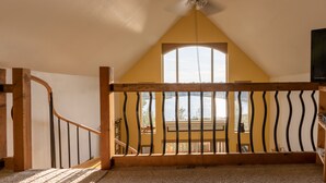 A room with a sloped ceiling, a wooden staircase, a balcony with a railing, and a ceiling fan.