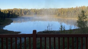 A calm lake with a forested shoreline and a wooden deck in the foreground.