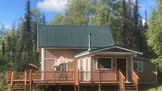 Une cabane à deux étages avec un toit végétalisé, une terrasse en bois et un grand parasol.