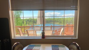 A dining table with two chairs, a window with a view of a deck and a lake, and a decorative item on the table.