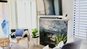 A modern living room with a fireplace, a flat-screen TV, and two grey armchairs. - Completely Remodeled, Full Tennis Privileges, ALWAYS Clean at Palm Valley CC!!   (Palm Desert)