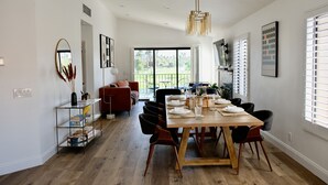A dining area with a wooden table set for four, surrounded by black chairs. There is a large window with blinds, a red sofa, and a bookshelf with books and decorative items. - Completely Remodeled, Full Tennis Privileges, ALWAYS Clean at Palm Valley CC!!   (Palm Desert)
