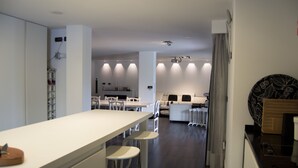 Una cocina moderna con una encimera larga, sillas blancas y una zona de comedor al fondo.