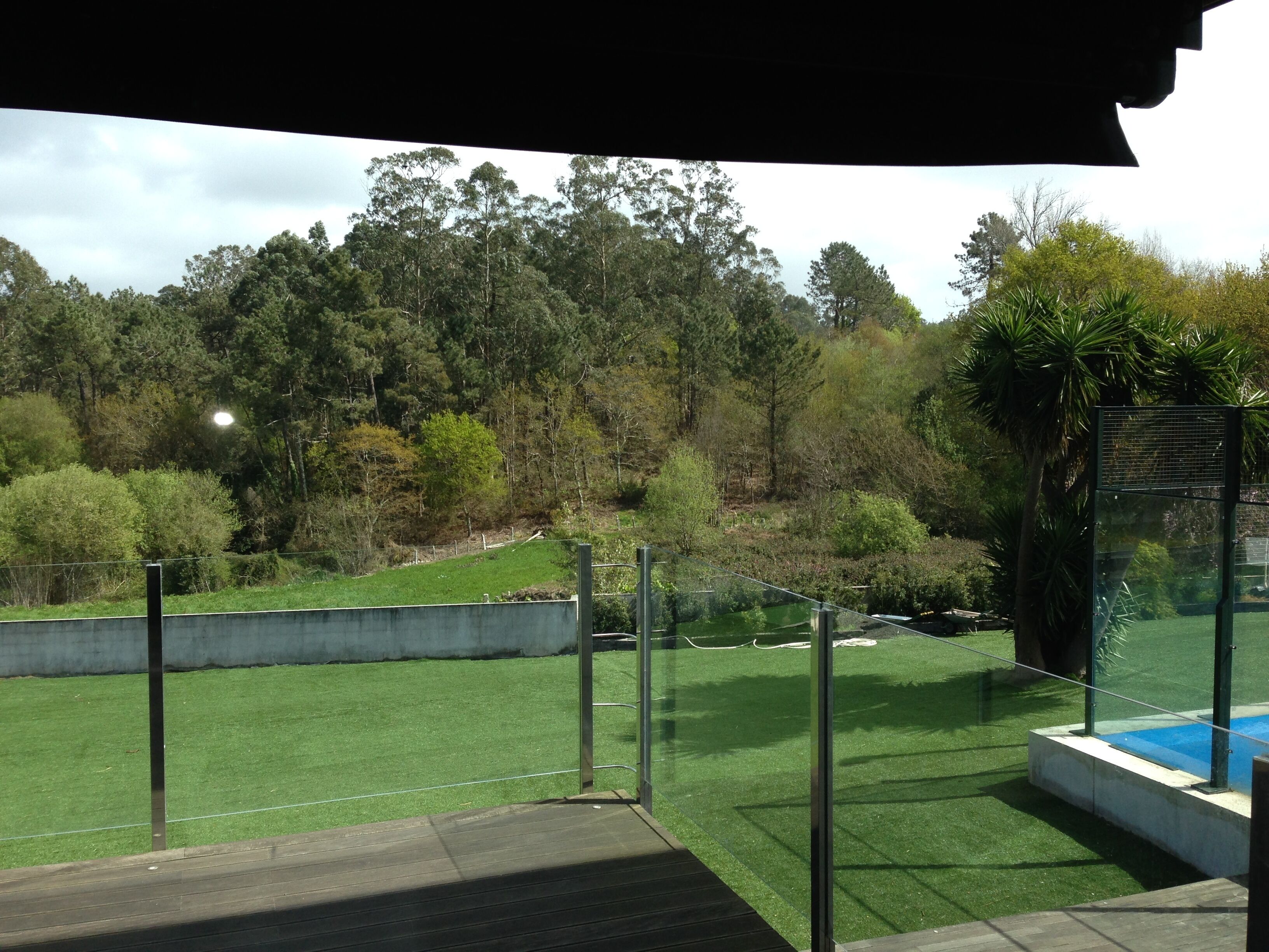 A view from a balcony with artificial grass, a pool, and a forested hillside.