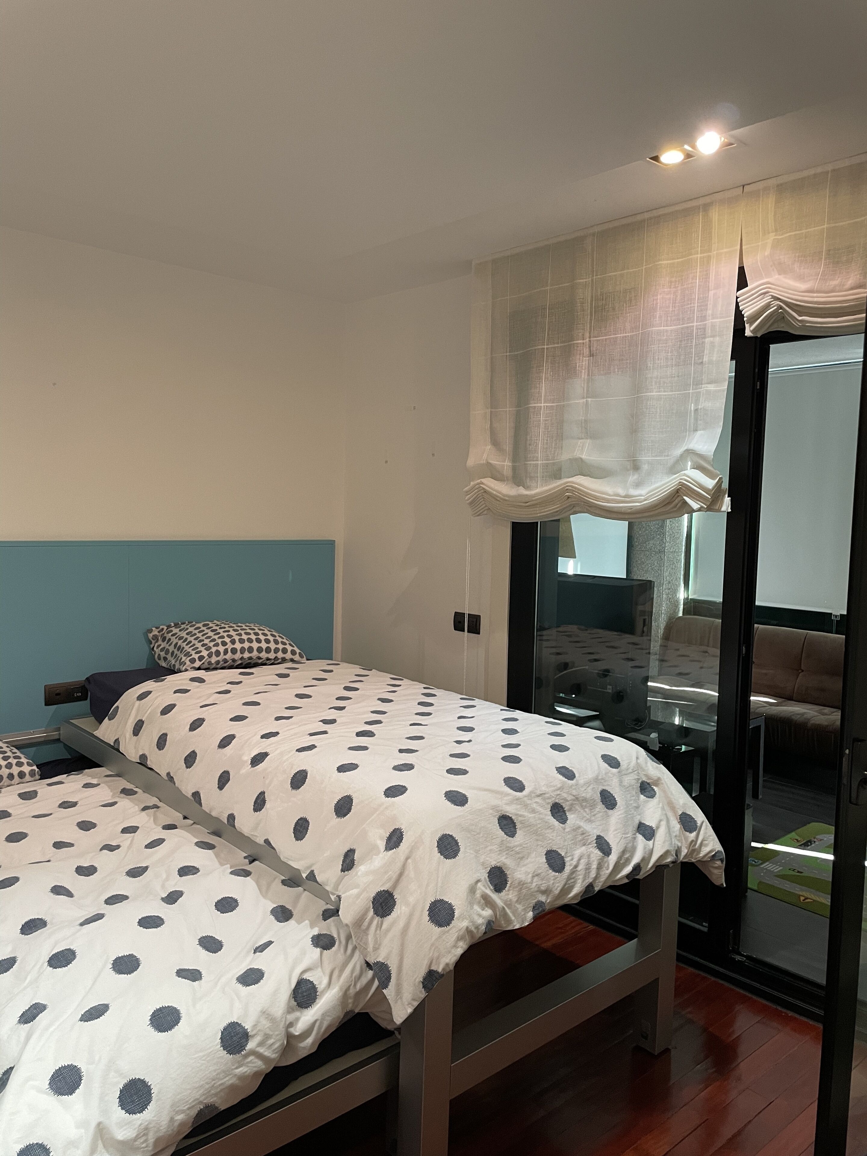 A bedroom with two beds, a large window with sheer curtains, and a view of a balcony.