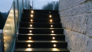 Una escalera con luces distribuidas uniformemente a lo largo de los peldaños, que conduce a una barandilla de vidrio.