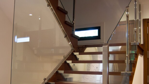 Una escalera moderna con barandillas de vidrio y peldaños de madera.