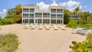 Ett hotell med utsikt över stranden, med en stor byggnad som har flera balkonger, en sandstrand framför och ett antal solstolar och bord.