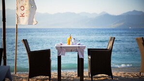 A beachside table with two wicker chairs, a flag, and a table set with a bottle and a napkin. - Ko Ko Mo Resort (Gili Trawangan)