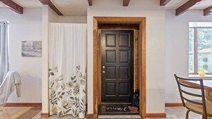 Une porte en bois à la teinte foncée, un paillasson blanc sur lequel est écrit le mot « bienvenue », et une fenêtre sur la droite.