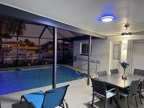 An outdoor pool area with a covered seating area, a table with chairs, and a ceiling fan. - Waterfront Property in the heart of beautiful Cape Coral, FL (Cape Coral)