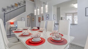 A dining area with a glass table set for six, white chairs, and a staircase with framed pictures. - Star Wars Villa - 10 Mins to Disney (Kissimmee)
