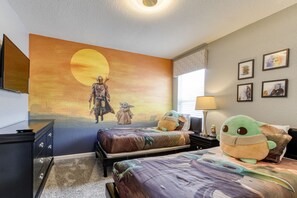 Quarto com um grande mural do pôr do sol, duas camas com roupa de cama temática de Star Wars e um brinquedo de pelúcia em uma das camas.