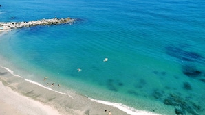 Een strand met helder turquoise water, een rotsenrij en een zandstrand.