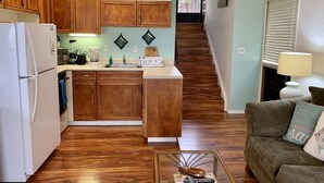 A kitchen with wooden cabinets, a white refrigerator, and a coffee maker. There is a staircase leading to a landing with a window.