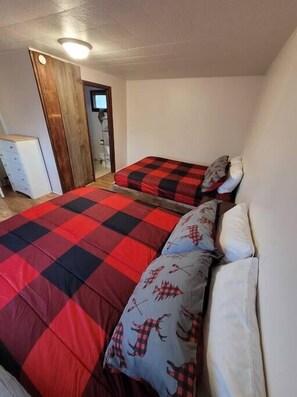A bedroom with two beds, a wooden wardrobe, and a small white cabinet. - Rustic Hook Lodge, Steelhead Suite (Wellston)
