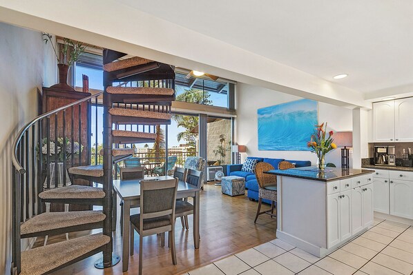 A spacious living area with a dining set, a blue sofa, and a kitchen with white cabinets.