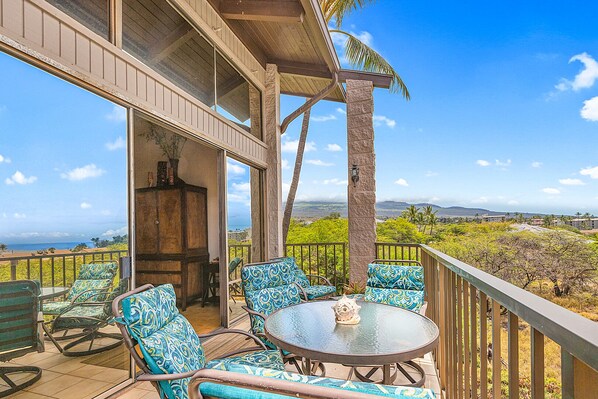 A balcony with a view of the ocean, furnished with chairs and a table.
