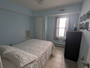 A bedroom with a bed, a wardrobe, a window with curtains, and a wall-mounted lamp. - 2 bedroom condo close to the boardwalk and attractions such as Jolly Roger (Ocean City)