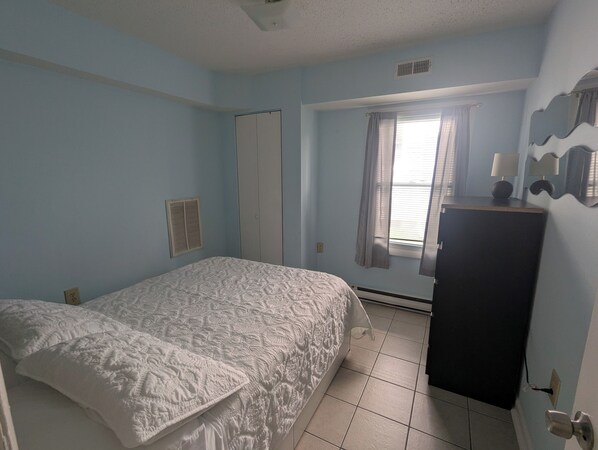 A bedroom with a bed, a wardrobe, a window with curtains, and a wall-mounted lamp.