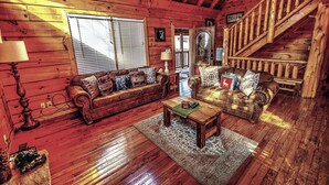 L’intérieur d’une cabane en rondins, avec deux canapés en cuir, une table basse en bois et un escalier.