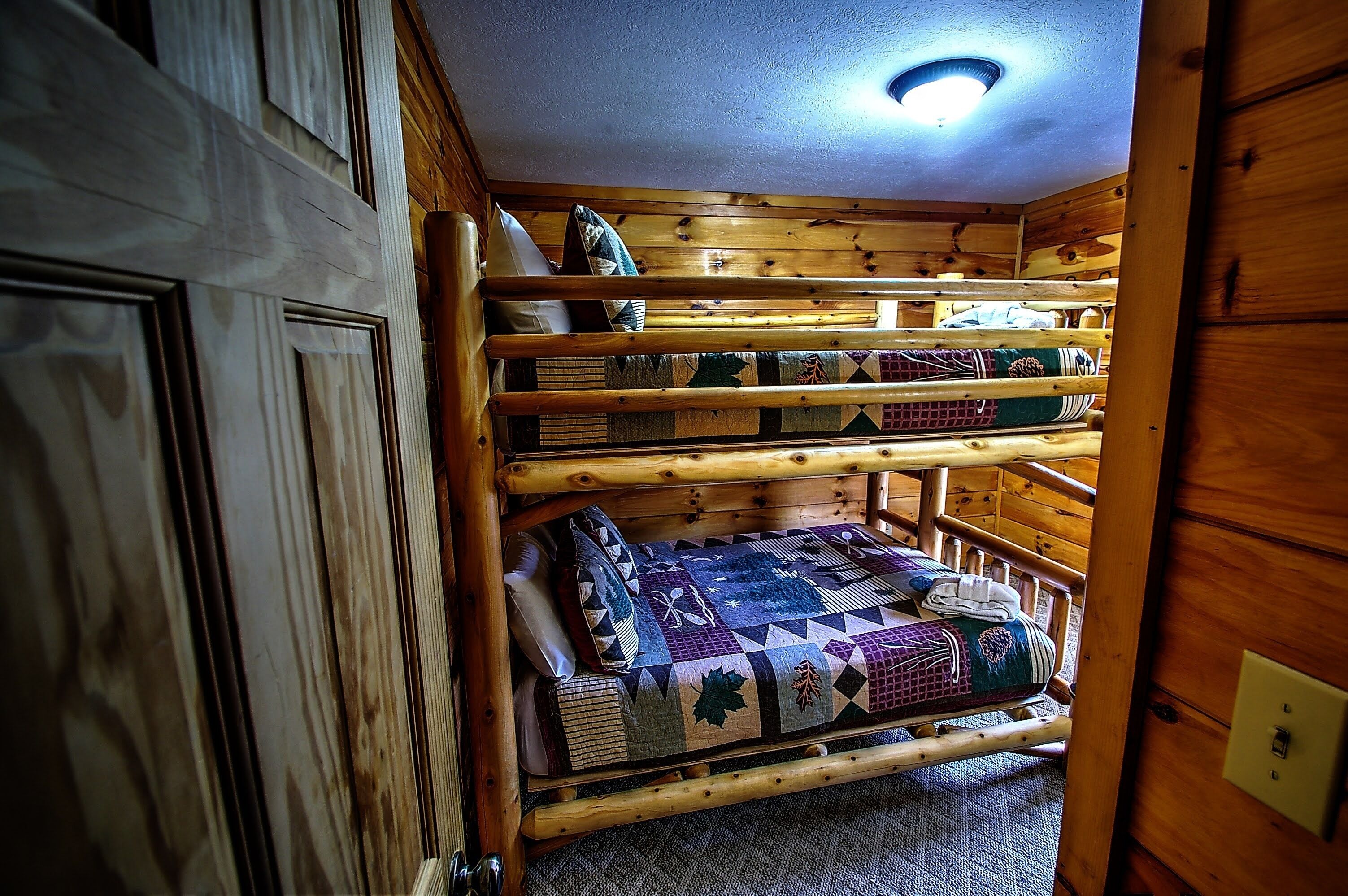 Une chambre avec des lits superposés à plusieurs niveaux, dotée de murs en bois et d’un luminaire au plafond.