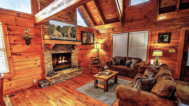 L’intérieur d’un chalet confortable, avec des murs en rondins de bois, une cheminée en pierre, des meubles en bois et une grande fenêtre.