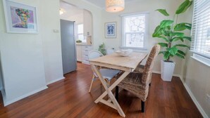 Un comedor con mesa de madera y sillas tejidas, una lámpara colgante y una planta en maceta.