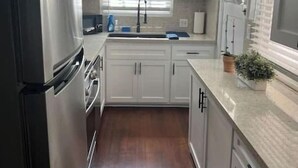 Una cocina moderna con armarios blancos, un refrigerador negro, un lavamanos y una ventana con persianas.