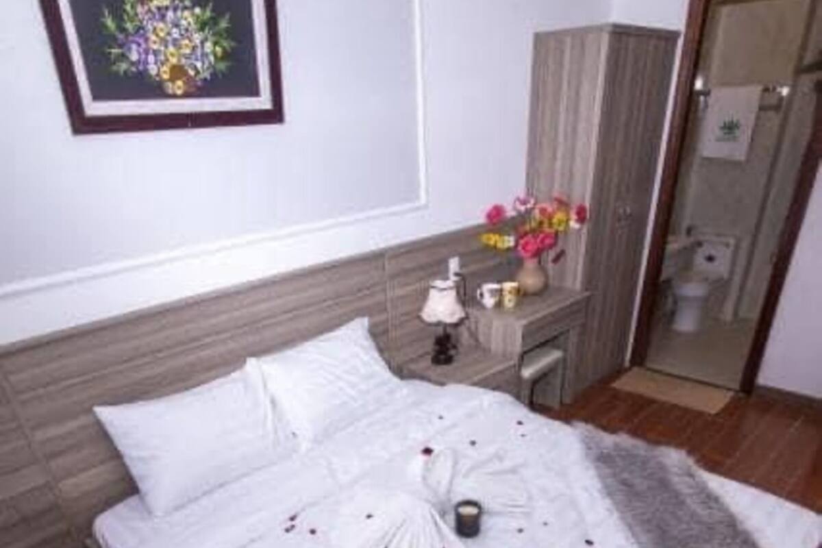 A neatly made bed with white linens, a bouquet of flowers on the nightstand, and a tray of fruit on the bed.