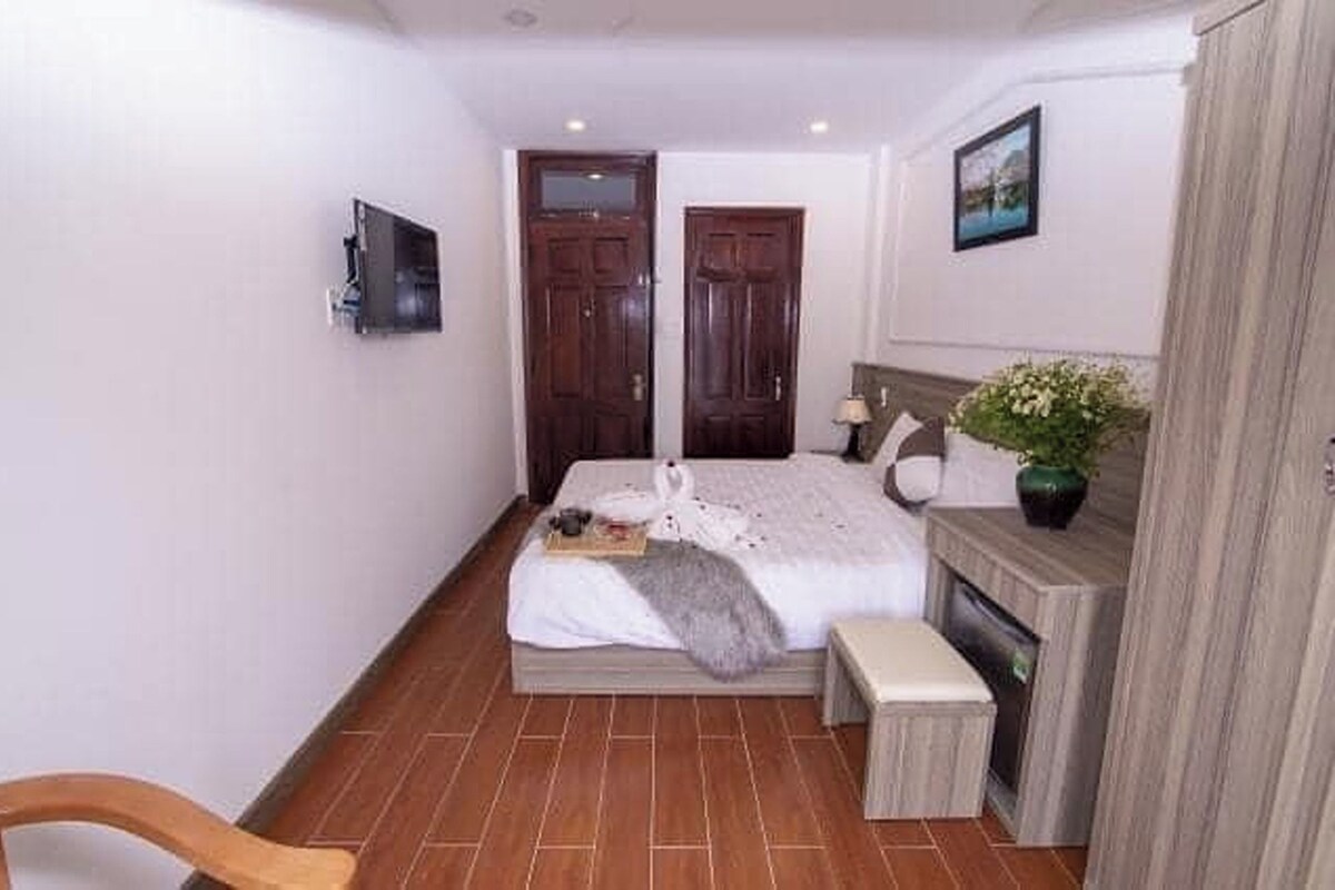 A bedroom with a bed, a small bedside table, a chair, a fireplace, and a wall-mounted TV.